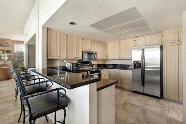 kitchen with cream cabinetry, stainless steel appliances, a breakfast bar, and kitchen peninsula