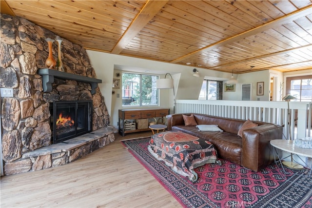 living room with light hardwood / wood-style floors, a stone fireplace, and wooden ceiling