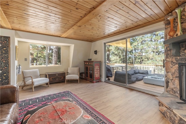 living area featuring beam ceiling, a stone fireplace, wood-type flooring, and wooden ceiling