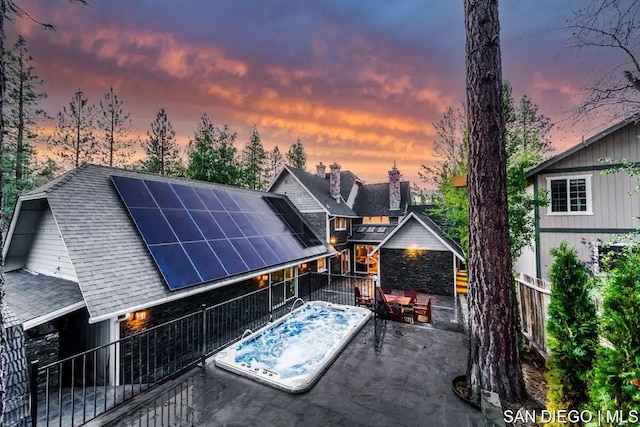 back house at dusk with solar panels and an outdoor hot tub