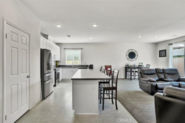 kitchen featuring white cabinetry, a kitchen bar, a peninsula, open floor plan, and stainless steel appliances