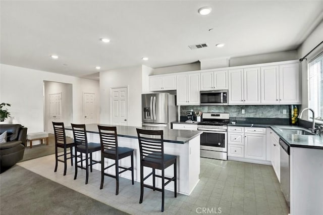 kitchen featuring a sink, a kitchen breakfast bar, dark countertops, stainless steel appliances, and visible vents