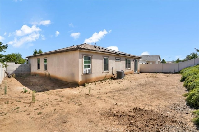 back of property with stucco siding, central air condition unit, a fenced backyard, and roof mounted solar panels