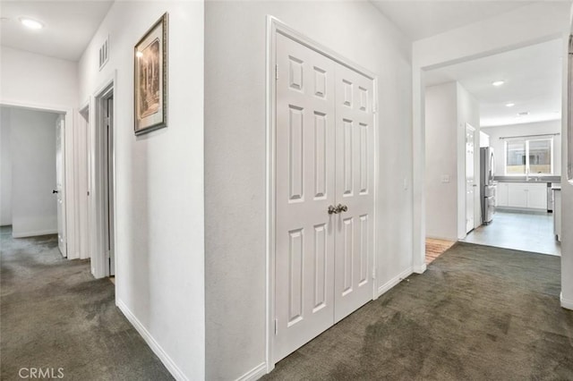 hallway with baseboards, visible vents, and dark colored carpet