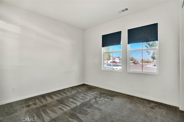 unfurnished room with baseboards, dark carpet, and visible vents