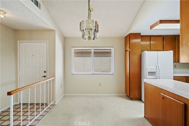 kitchen with a textured ceiling, tile countertops, a notable chandelier, hanging light fixtures, and white fridge with ice dispenser