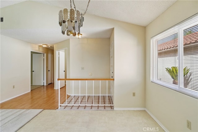 unfurnished room with a textured ceiling, light hardwood / wood-style floors, vaulted ceiling, and an inviting chandelier