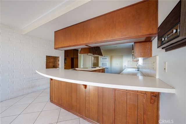 kitchen with kitchen peninsula, light tile patterned floors, sink, and brick wall