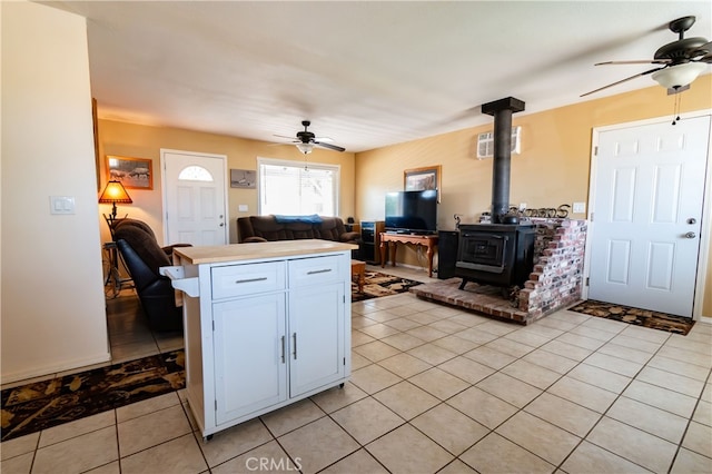 kitchen with a wood stove, kitchen peninsula, ceiling fan, white cabinets, and light tile patterned floors