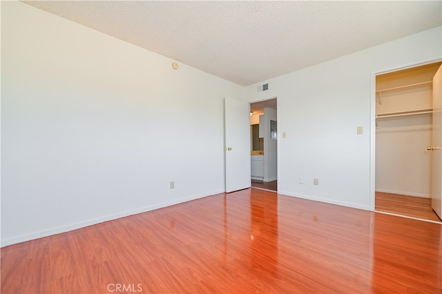 unfurnished bedroom featuring a textured ceiling, a walk in closet, wood-type flooring, and a closet