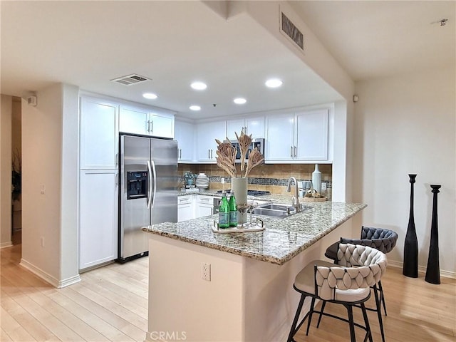 kitchen featuring white cabinets, stainless steel fridge, light stone counters, and kitchen peninsula