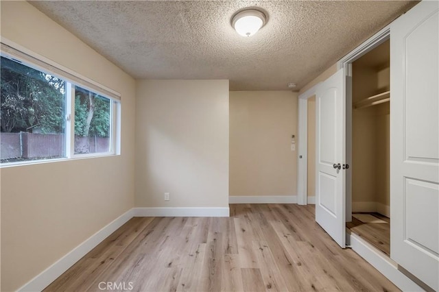 unfurnished bedroom with a closet, baseboards, light wood-type flooring, and a textured ceiling