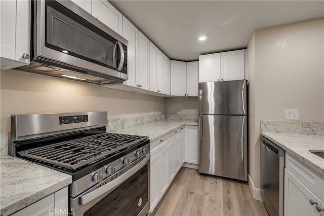 kitchen with white cabinetry, light stone counters, stainless steel appliances, and light wood-type flooring