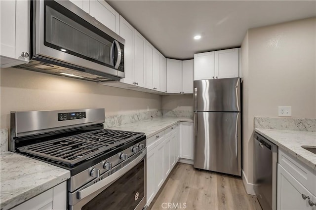 kitchen with light wood-style floors, appliances with stainless steel finishes, white cabinetry, and light stone countertops