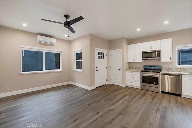kitchen with stainless steel appliances, a wall mounted AC, light wood-style flooring, and a ceiling fan