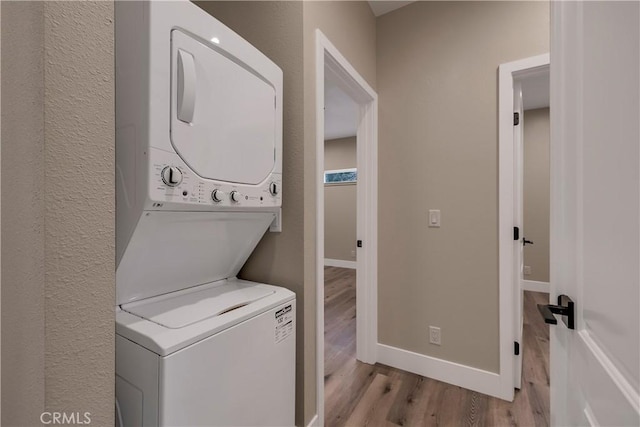 laundry area with light wood-style flooring, laundry area, baseboards, and stacked washer / drying machine