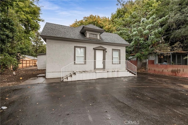 bungalow-style home featuring roof with shingles, stucco siding, and fence
