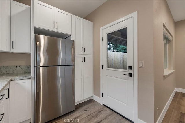 kitchen featuring baseboards, light stone counters, freestanding refrigerator, white cabinets, and light wood finished floors