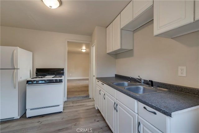 kitchen with light wood-style floors, a sink, white appliances, and dark countertops