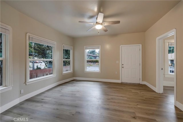 empty room featuring a wealth of natural light, baseboards, a ceiling fan, and wood finished floors