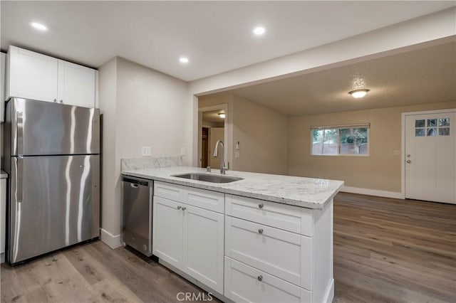 kitchen with a peninsula, white cabinetry, stainless steel appliances, light wood finished floors, and a sink