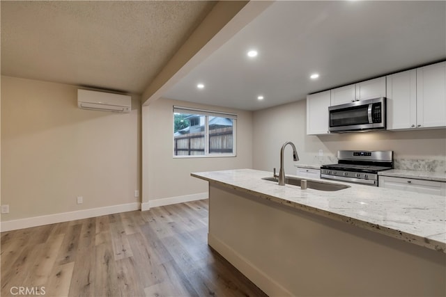 kitchen featuring light stone countertops, a wall mounted air conditioner, sink, light hardwood / wood-style floors, and stainless steel appliances