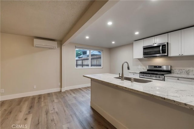 kitchen with stainless steel appliances, a wall mounted AC, a sink, and light stone counters