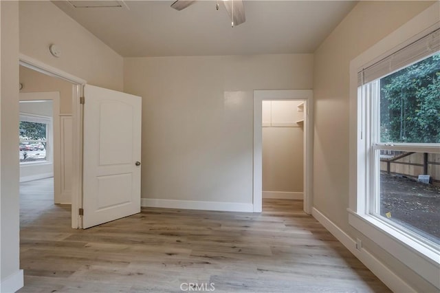 unfurnished bedroom with light wood-style flooring, baseboards, multiple windows, and a walk in closet