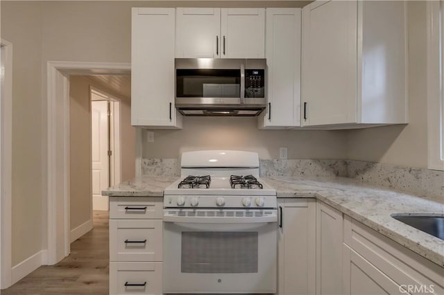 kitchen featuring white range with gas cooktop, light stone countertops, light wood-style flooring, white cabinets, and stainless steel microwave