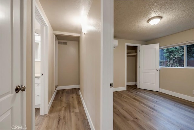 hall with baseboards, light wood-style flooring, a textured ceiling, visible vents, and a wall unit AC
