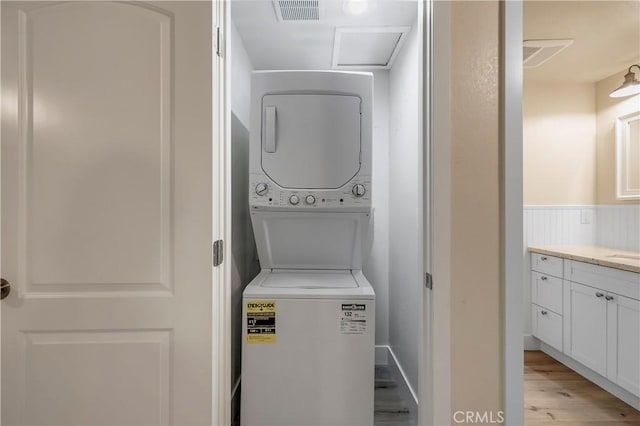 laundry room featuring stacked washer / dryer, laundry area, light wood finished floors, and visible vents
