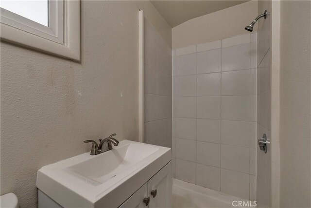bathroom with tiled shower, vanity, and toilet