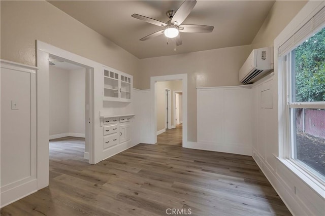 interior space with ceiling fan, a wall unit AC, and wood finished floors