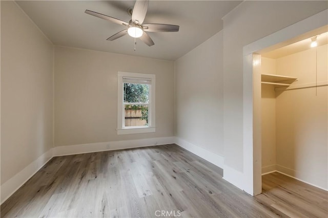 unfurnished bedroom featuring a closet, baseboards, a ceiling fan, a walk in closet, and wood finished floors
