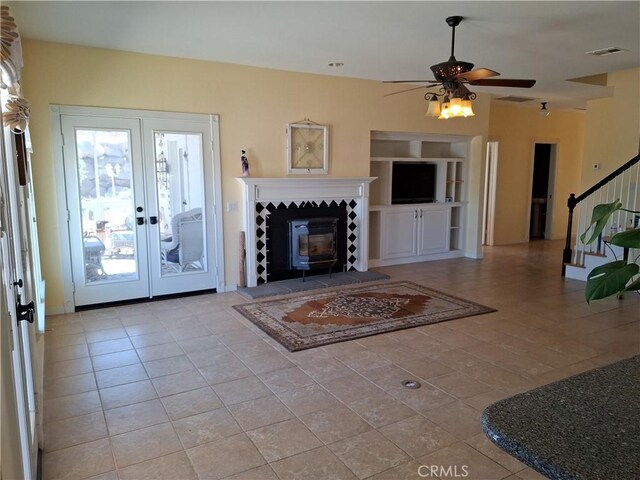 tiled living room featuring french doors, built in shelves, a wood stove, and ceiling fan