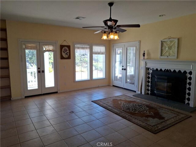 unfurnished living room featuring french doors, light tile patterned flooring, a tile fireplace, and ceiling fan