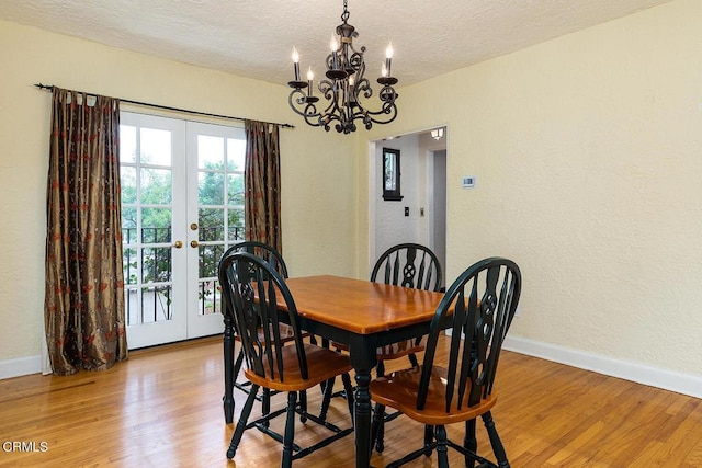 dining space with a notable chandelier, light hardwood / wood-style floors, a textured ceiling, and french doors