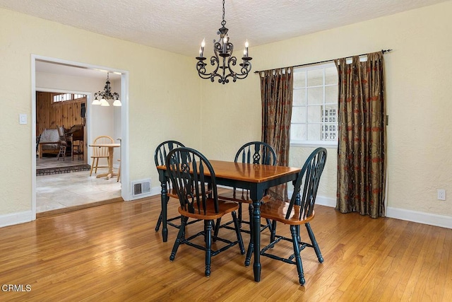 dining room with an inviting chandelier, a textured ceiling, and light hardwood / wood-style flooring