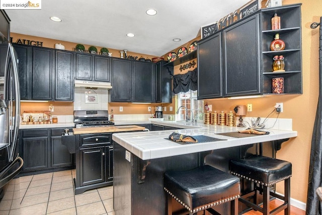 kitchen featuring stainless steel appliances, tile counters, sink, and a breakfast bar area