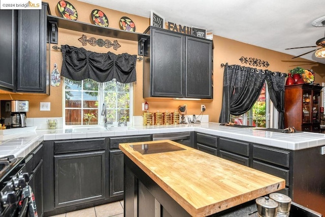 kitchen with ceiling fan, a kitchen island, tile counters, and range with gas cooktop