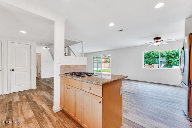 kitchen with light brown cabinets, light stone counters, ceiling fan, light hardwood / wood-style floors, and stainless steel appliances