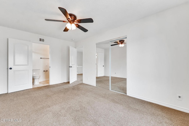 unfurnished bedroom with a closet, ensuite bathroom, light colored carpet, and ceiling fan