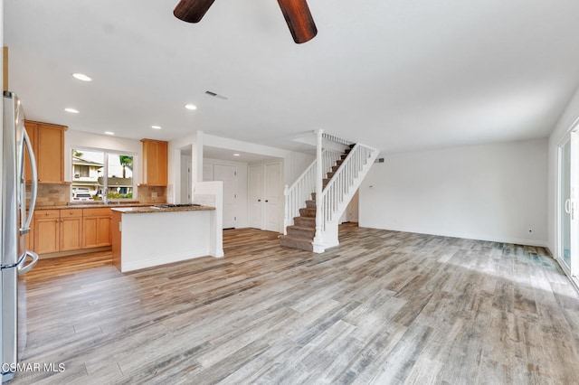 kitchen with light brown cabinets, stainless steel fridge, light wood-type flooring, and backsplash