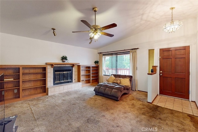 carpeted living room with lofted ceiling, a tile fireplace, and ceiling fan with notable chandelier