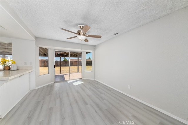 unfurnished living room with a textured ceiling, light wood-type flooring, and ceiling fan