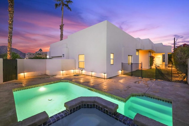 pool at dusk featuring a patio area and an in ground hot tub