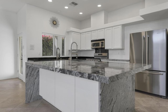 kitchen with a spacious island, sink, dark stone countertops, stainless steel appliances, and white cabinets