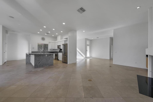 kitchen with light tile patterned flooring, sink, appliances with stainless steel finishes, an island with sink, and white cabinets