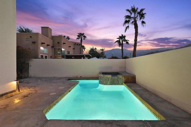 pool at dusk featuring an in ground hot tub, a mountain view, and a patio area