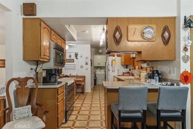 kitchen with kitchen peninsula, washer / clothes dryer, a breakfast bar, and black appliances